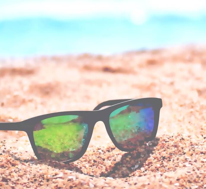 A pair of sunglasses sitting on the sand at the beach.