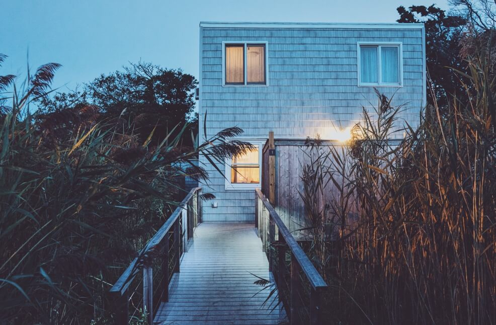 A wooden walkwya leads up to the front door of a beachfront cottage at night.